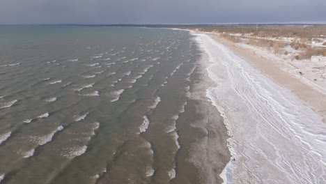 A-serene,-sandy-beach-with-gentle-waves-and-clear-skies,-coastline-stretching-into-the-distance,-aerial-view