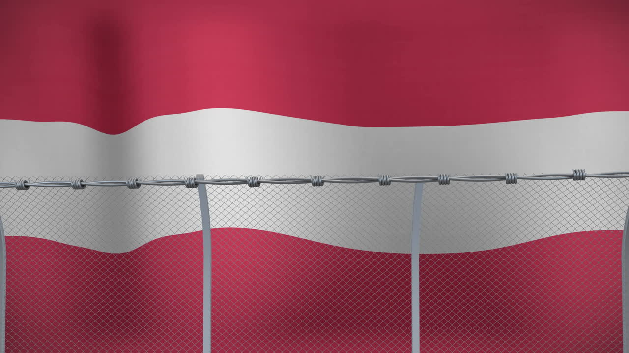 라트비아 국기가 가시선으로 된 금속 울타리 위에 흔들리고 있습니다.