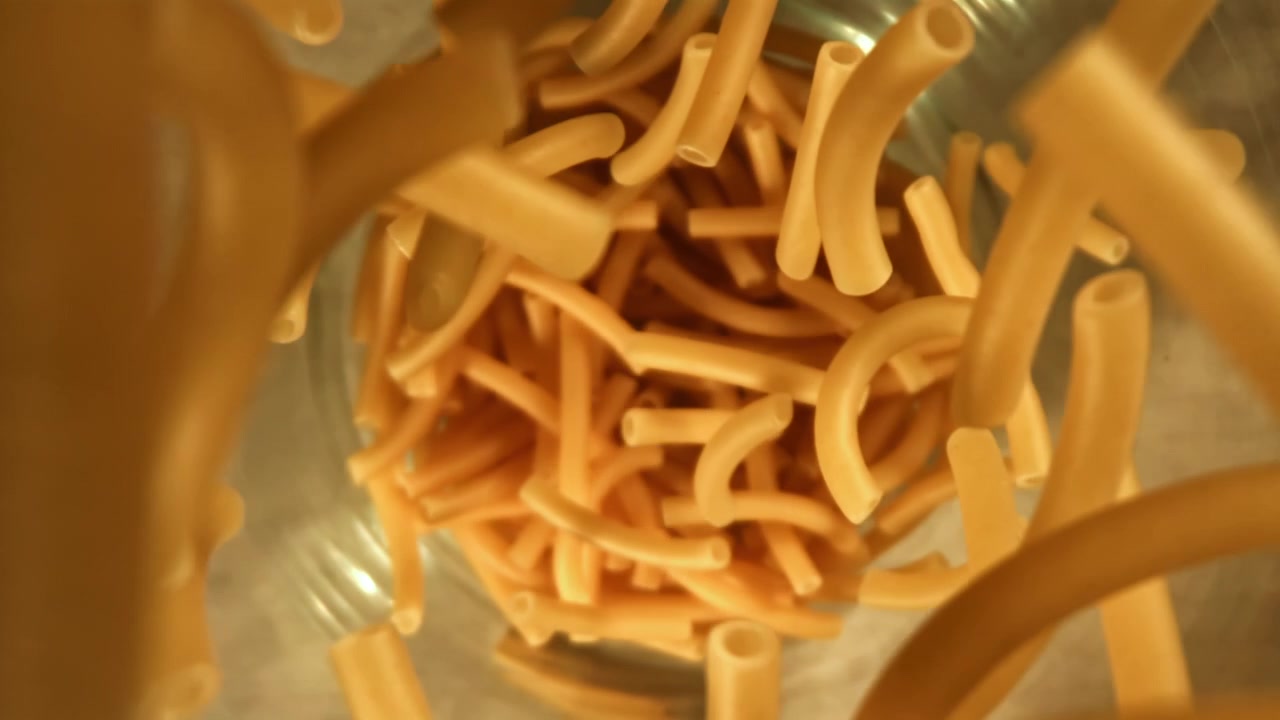 スローモーションで容器に落ちる乾燥マカロニパスタ