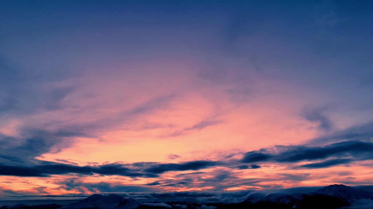 Wide view of a dramatic sunset sky with warm pink and orange tones blending into deep blue clouds, creating a calm and atmospheric evening scene
