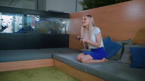 woman gaming and relaxing in modern office. young formal woman in skirt chilling on sofa in contemporary office recreation area and playing videogame with gamepad