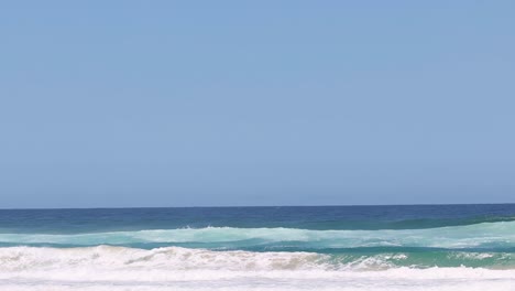 a series of gentle ocean waves roll steadily under a bright, clear blue sky.