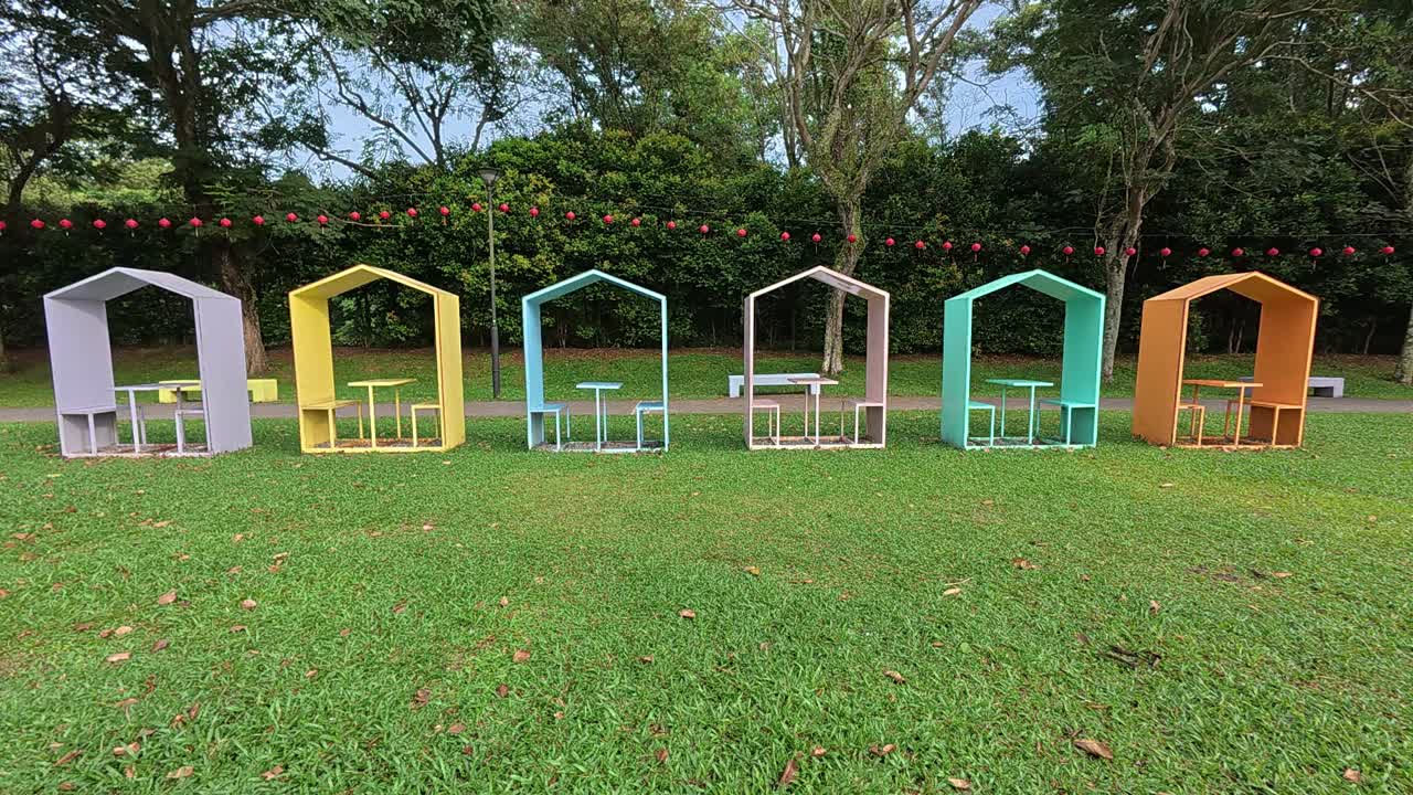 This video showcases colorful, covered benches in a Malaysian public park, neatly arranged in a row. Each bench accommodates two people, providing a shaded and inviting spot for relaxation.
