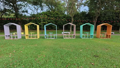 this video showcases colorful, covered benches in a malaysian public park, neatly arranged in a row. each bench accommodates two people, providing a shaded and inviting spot for relaxation.