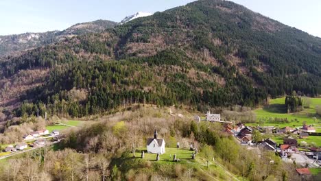 drone shot of a chapel on top of a hill in front of alpine mountains