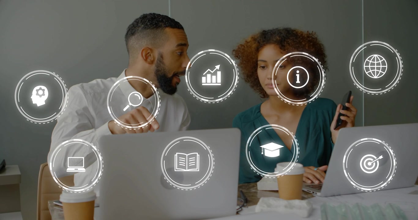 Man leaning, pointing at laptop, sparking tech icons overlaying grid between pair planning work