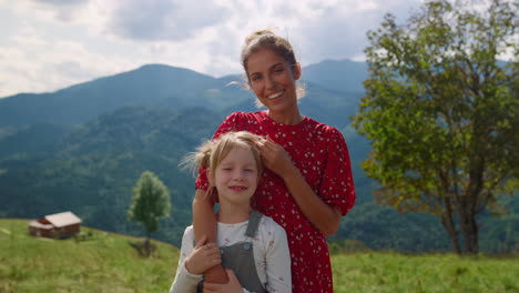 Mother-stroking-girl-head-standing-in-front-mountains-closeup.-Family-holiday.