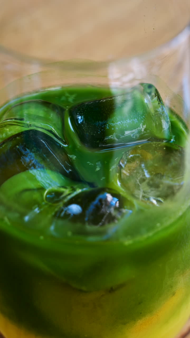 Close up of a glass of an iced orange juice matcha on a table at a cafe. Vertical