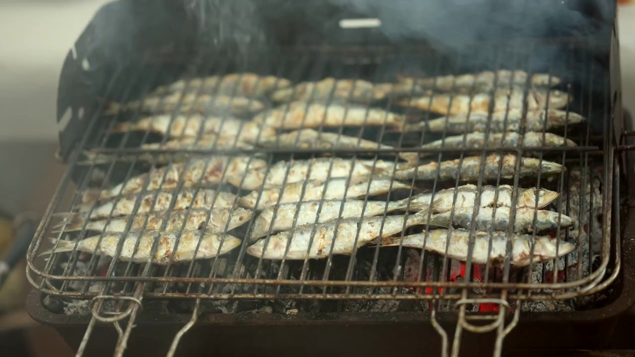 Sardine intere fresche che cuociono su una griglia a carbone ardente, con il fumo che infonde sapore. Preparazione di pesce sana e tradizionale