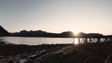 flying at the shore through a fish rack then flying towards the setting sun behind the mountains and the shallow water