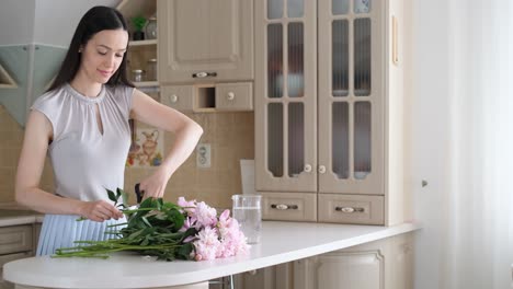 Smiling Young Creative Woman Decorates House with Flowers while Standing at Table Smiling Young Creative Woman Decorating the House with Flowers while Standing at the Table Fresh Cut Flowers for Decoration Home