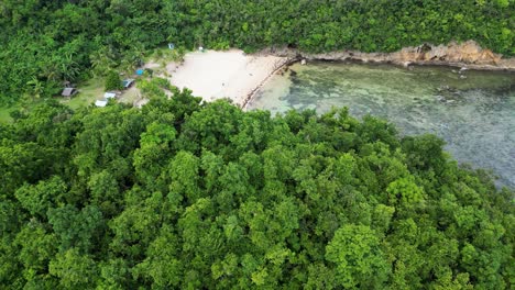 Vista-Aérea-Cinematográfica-De-Una-Colina-Cubierta-De-árboles-Que-Revela-Un-Resort-De-Playa-De-Arena-Blanca-Escondido-Con-Impresionantes-Aguas-Claras