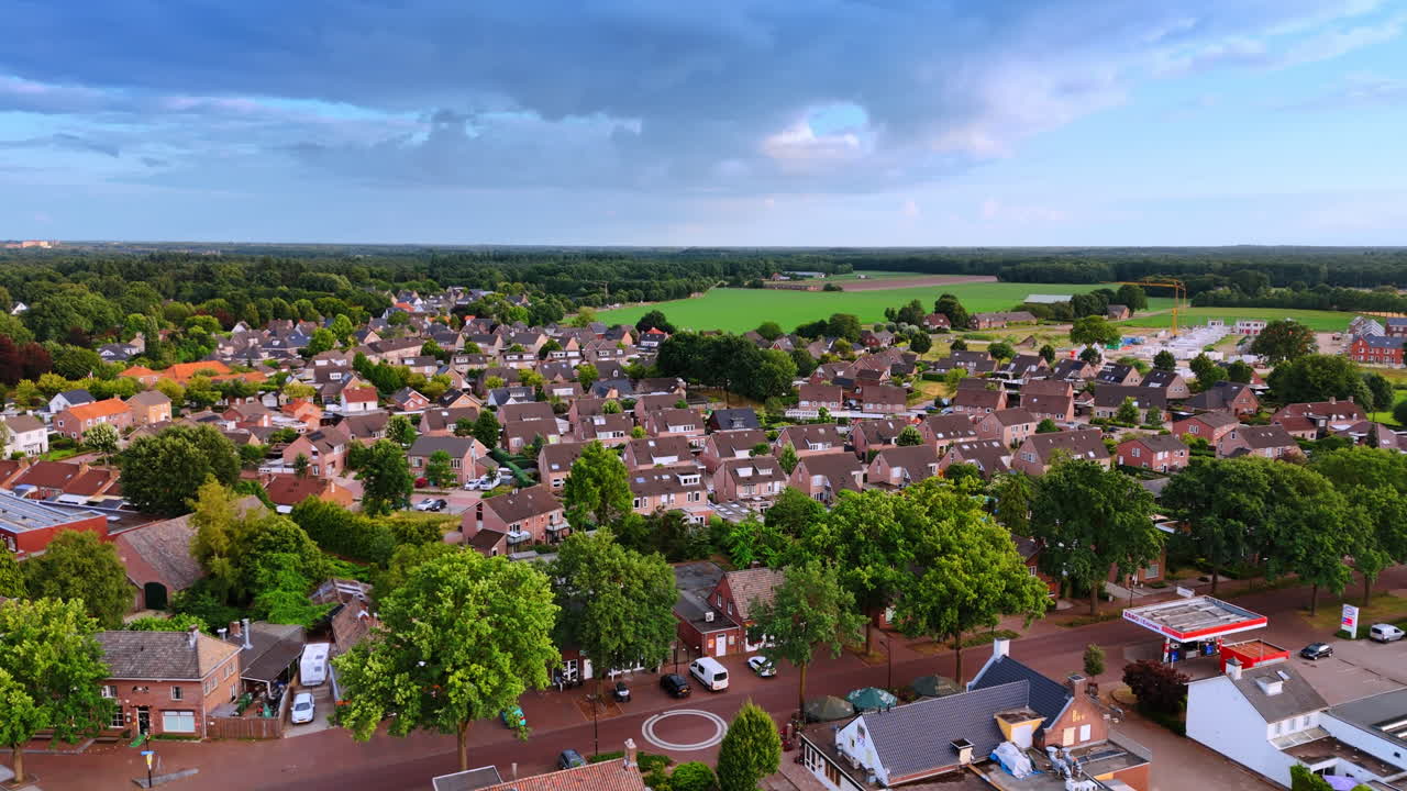 Udsigt fra oven over et byområde nær grønne marker. Panoramisk luftfoto af et boligområde med murstenshuse, gader, lokal tankstation og et stort landbrugsfelt.