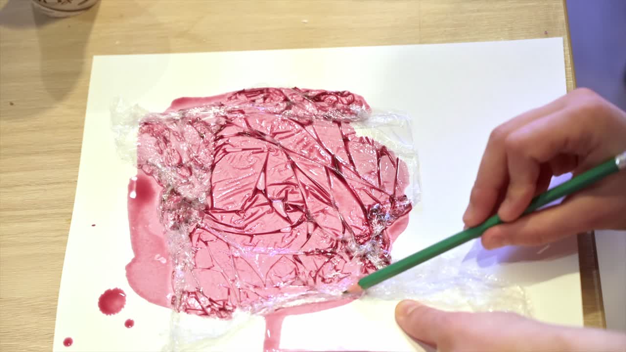 Una donna in uno studio dipinge su carta con vino rosso e cellophane, vista ravvicinata, slow motion