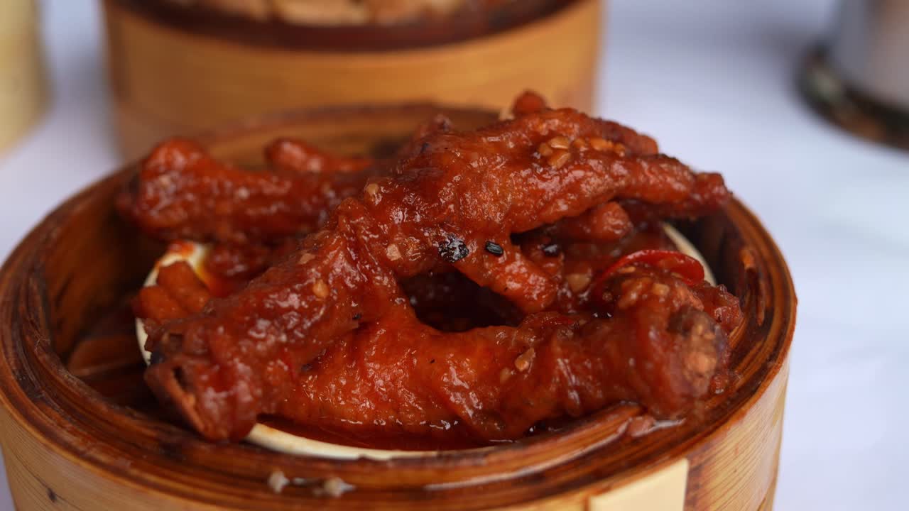 Close up shot of a traditional dim sum dish, featuring braised chicken feet in rich, dark red sauce, served in bamboo steamer at the restaurant.