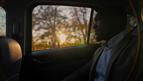 Side-view-of-a-male-businessman-with-Black-skin-with-a-beard-rides-in-a-car-during-his-business-trip-outside-an-urban-area-on-a-sunny-evening-at-sunset