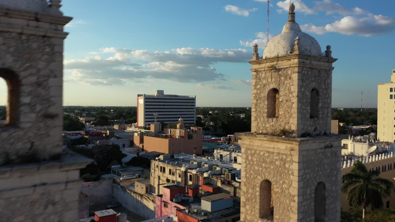 cámara aérea al atardecer deslizándose hacia la derecha y levantándose detrás de los campanarios de la rectoría jesús en merida, yucatan, mexico