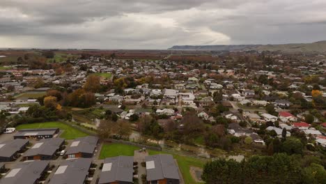aerial drone view over the suburban town of blenheim, south island, new zealand, showing residential houses, trees, and distant fields under a cloudy sky. community landscape