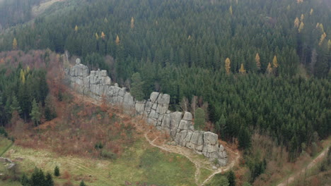 aerial shot of hiking trails along rock wall in a pristine forest, green trees in a valley