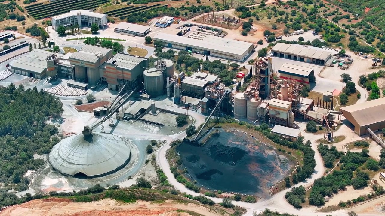 Limestone quarry operations extract raw materials. Heavy machinery transports aggregates. Conveyor belts move materials through the site. Aerial view reveals industrial manufacturing complex layout.