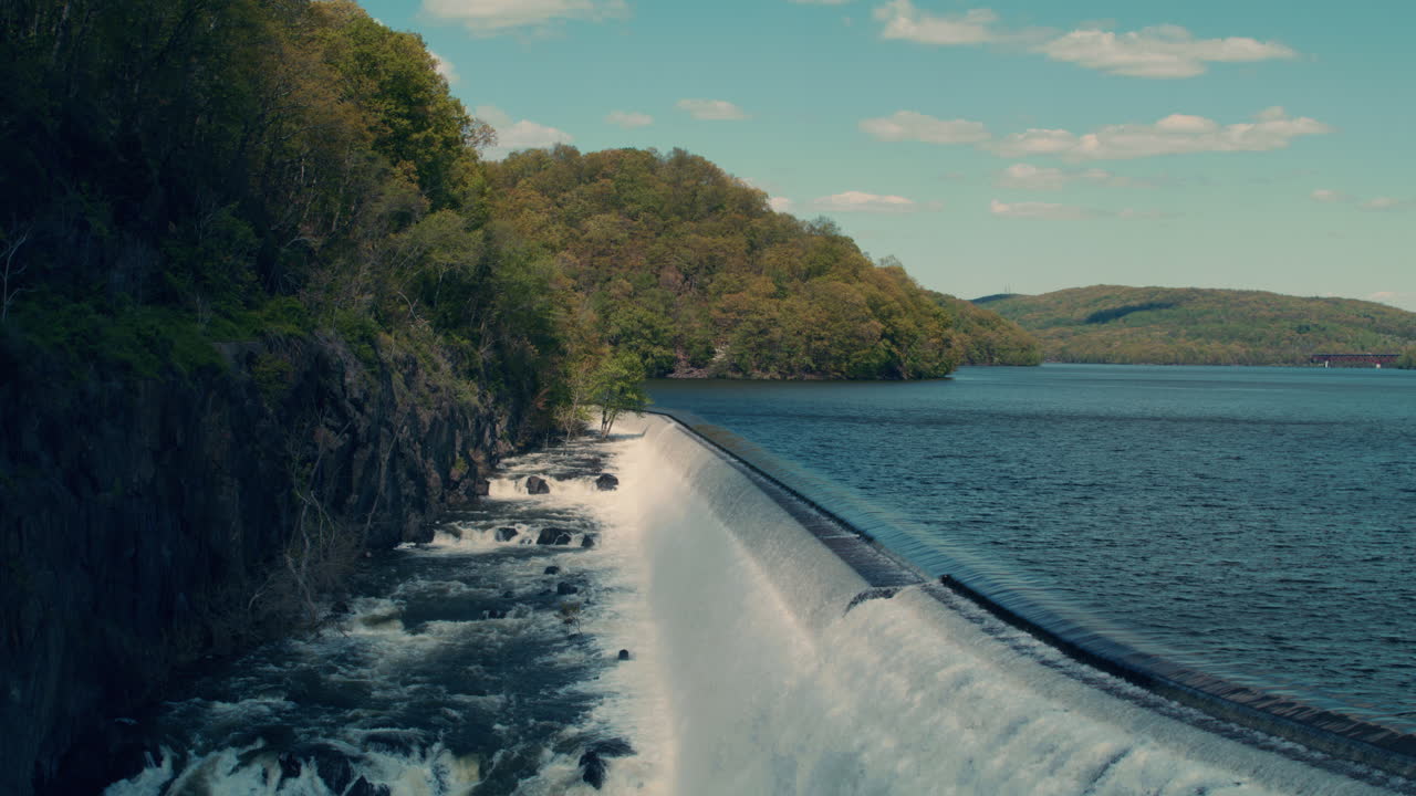 wide shot of new croton reservoir stepped spillway and gorge with lake, mountains and blue sky in the background. slow motion 40fps