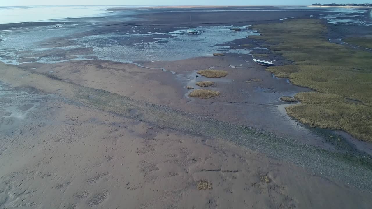 Drone flight out to sea. starting low, flying over beached boats on mud flat during low tide. This shows the different habitats the coastline provides.