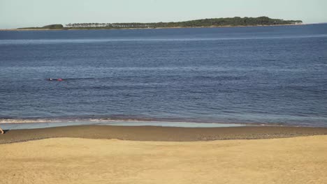 Woman-walking-on-beach-with-swimmer-in-the-sea