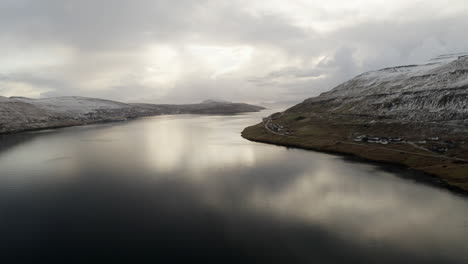 Faroe-Islands,-4K-Aerial-of-town-perched-on-the-edge-of-the-water-with-beautiful-cloud-and-sunshine-reflections