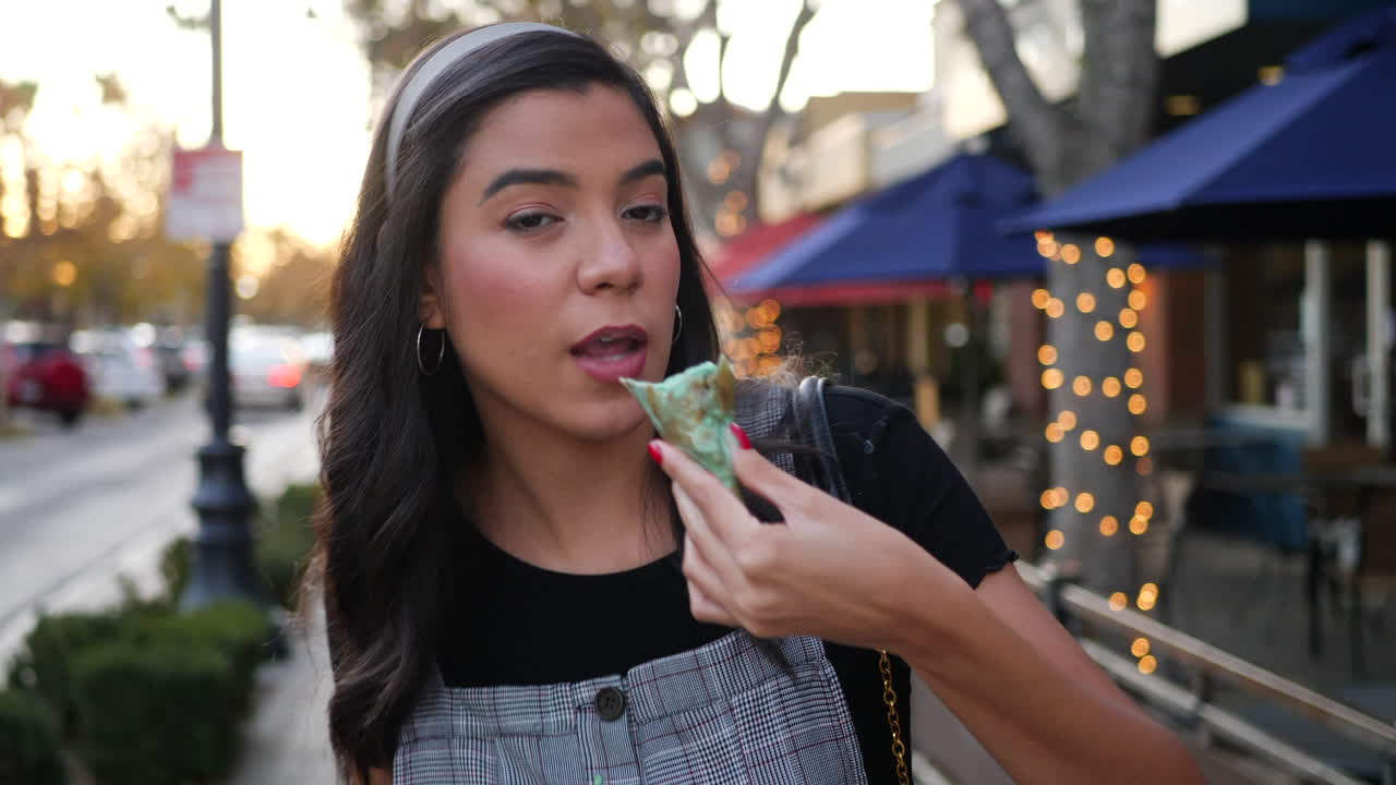 A beautiful young hispanic woman laughing and eating a messy, dripping ice cream cone dessert on the city street at sunset SLOW MOTION