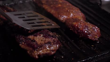 spatula flipping beef steaks from raw to cooked charred sides, closeup