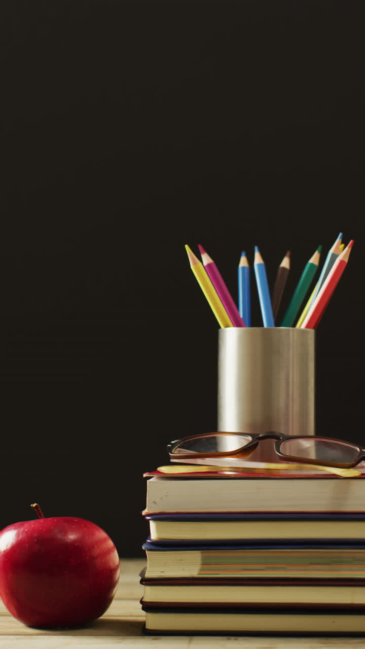video vertical de una pila de libros, lápices de colores y manzana sobre fondo negro