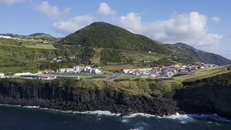 Velas,-Insel-Sao-Jorge,-Azoren,-Portugal-Luftbild-Von-Weiß-Getünchten-Häusern,-Dorf,-Skatepark,-Sportplatz,-Mit-Umliegenden-Bergen,-Vegetation-Und-Lavaformationen-Drohnenaufnahmen-Am-Meer