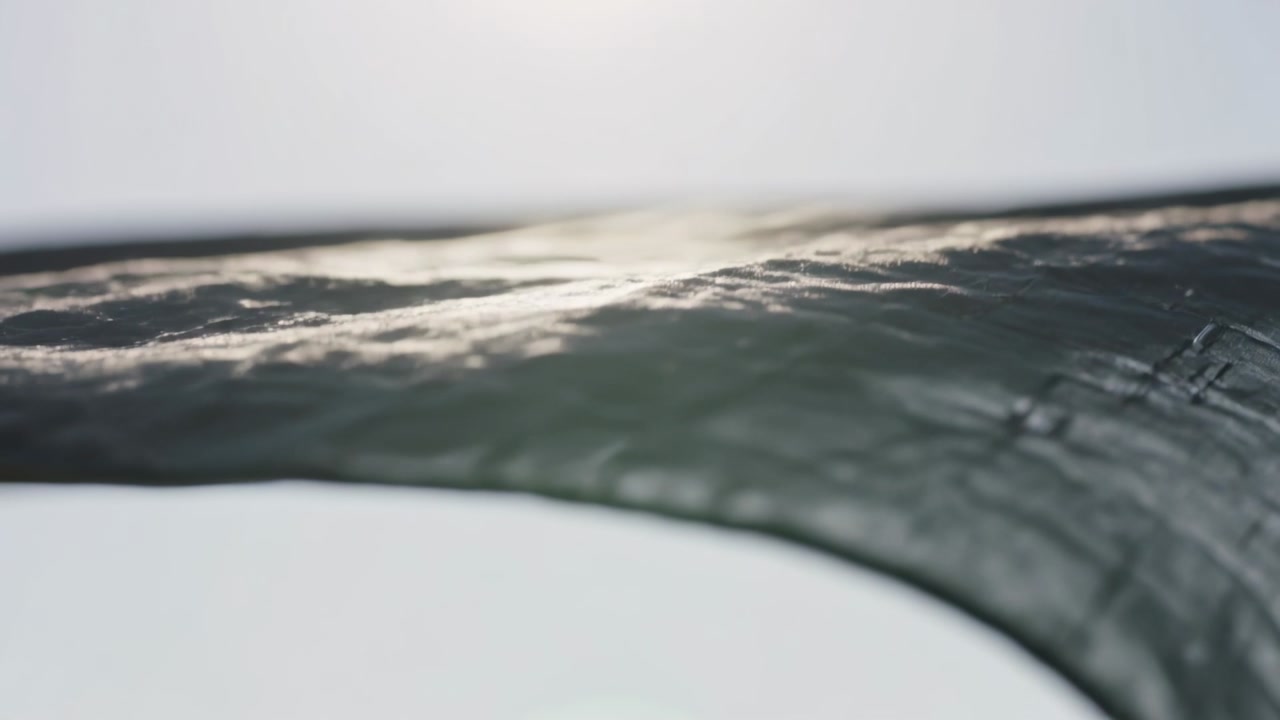 Camera moving along curved dark textured sheet in studio, tracing rim and revealing scuffed surface