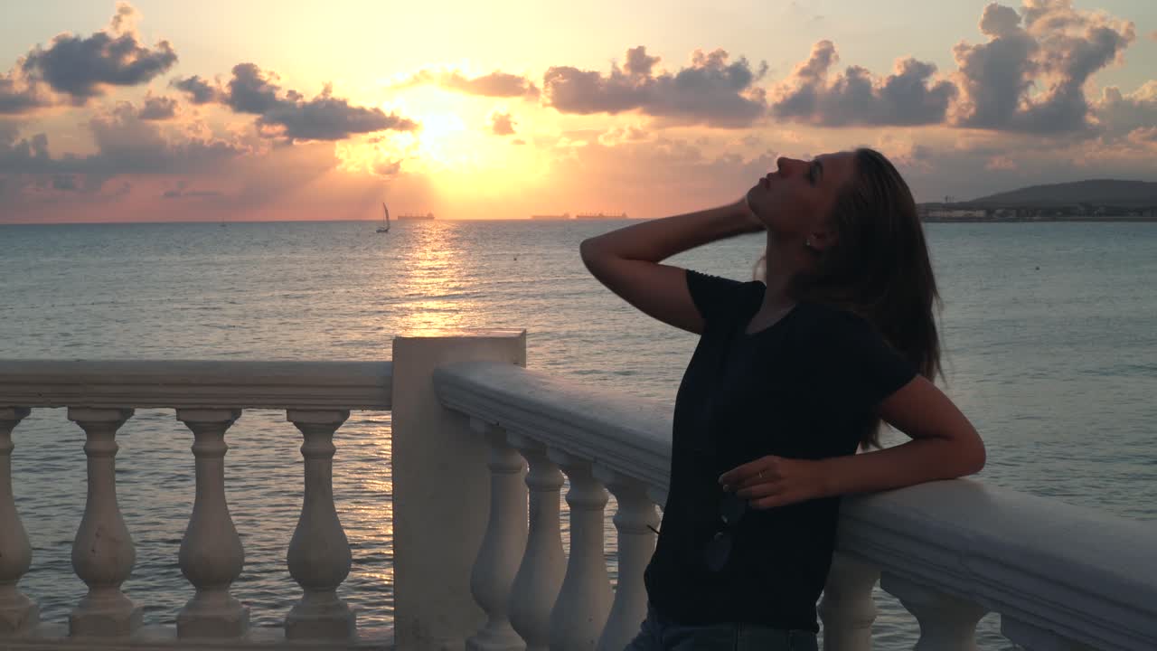 발코니 에서 바다 위 의 해가 지는 것 을 지켜보고 있는 여자