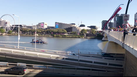 barge travels up brisbane river towards grey st bridge with the wheel of brisbane and south bank in distance