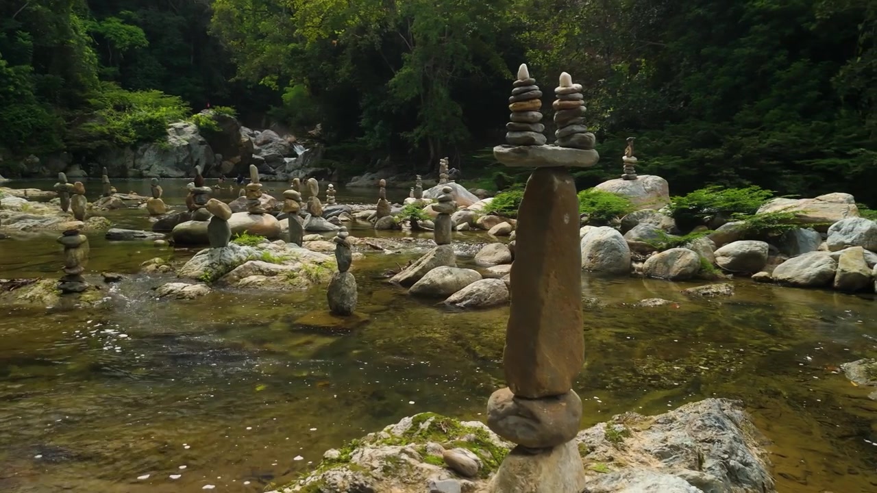 Molti cairn di pietre bilanciate e torri di roccia impilate posizionati su massi lungo il fiume poco profondo e limpido Poza Encantada, in mezzo a una giungla lussureggiante vicino a Santa Marta, Colombia
