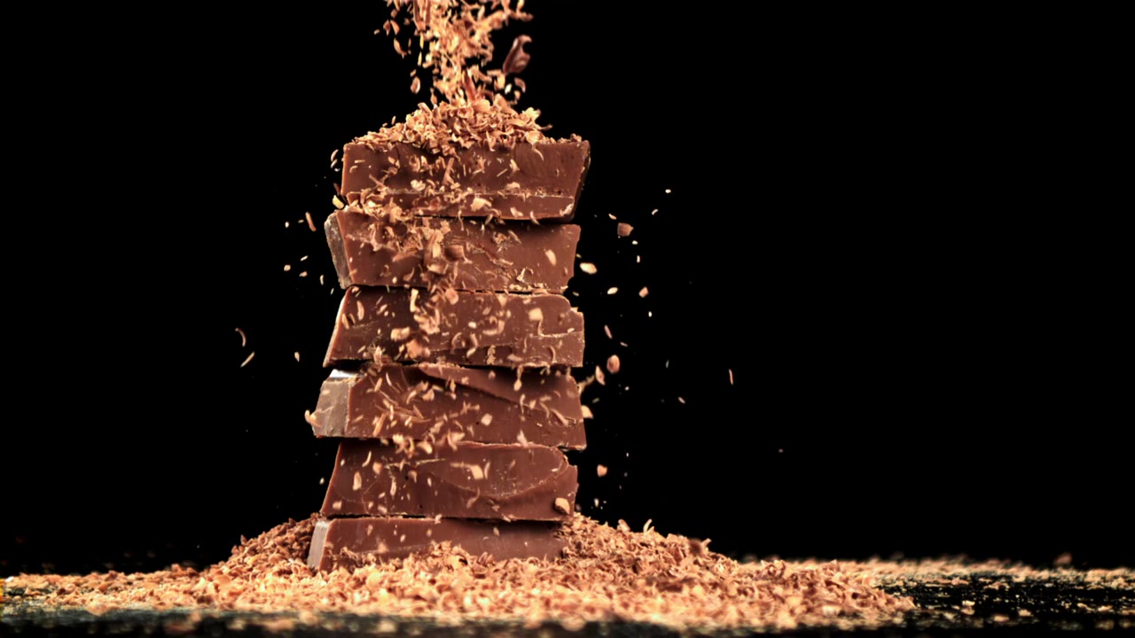 Raspas de Chocolate Caindo em Câmera Lenta sobre Pedaços de Chocolate Empilhados