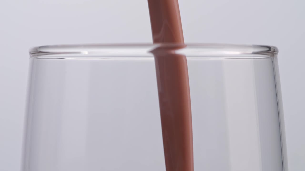 Primo piano di bevanda al latte al cioccolato versata al rallentatore in un bicchiere tumbler su sfondo bianco