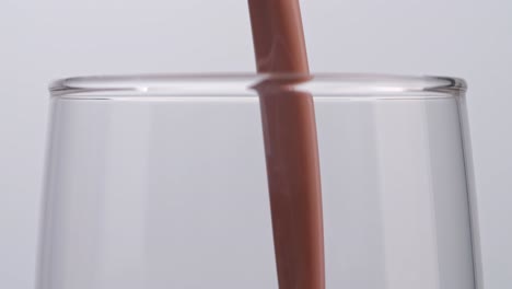 close up of slow motion pour chocolate milk drink in tumbler glass on white background