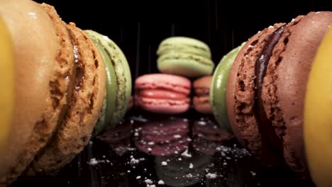 reverse moving macro view past macarons with powdered sugar falling on black reflective glass, luxury french pastries, sweet sugary food