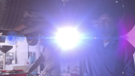 women mechanics inspecting car undercarriage in automotive repair garage, with floating chart icons