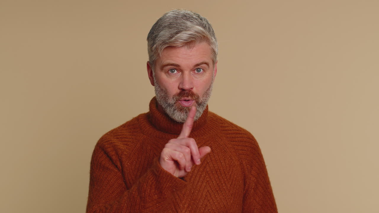 Senior man presses index finger to lips makes silence gesture sign do not tells secret shh be quiet