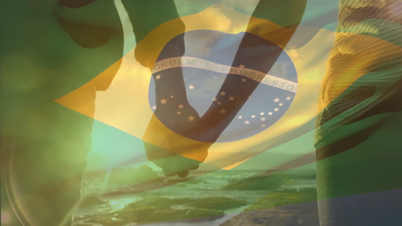 Animation of waving brazil flag against mid section of couple holding hands walking on the promenade
