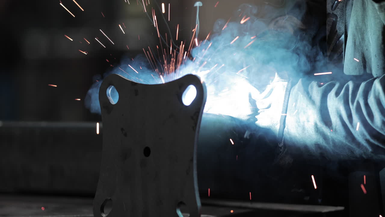 рабочий аккуратно сваривает металл на заводе - тепло и искры от сварочного инструмента - замедленная съемка крупным планом