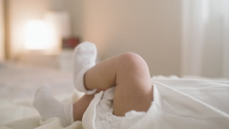 vista de cerca de las piernas de un bebé acostado en la cama con botines blancos