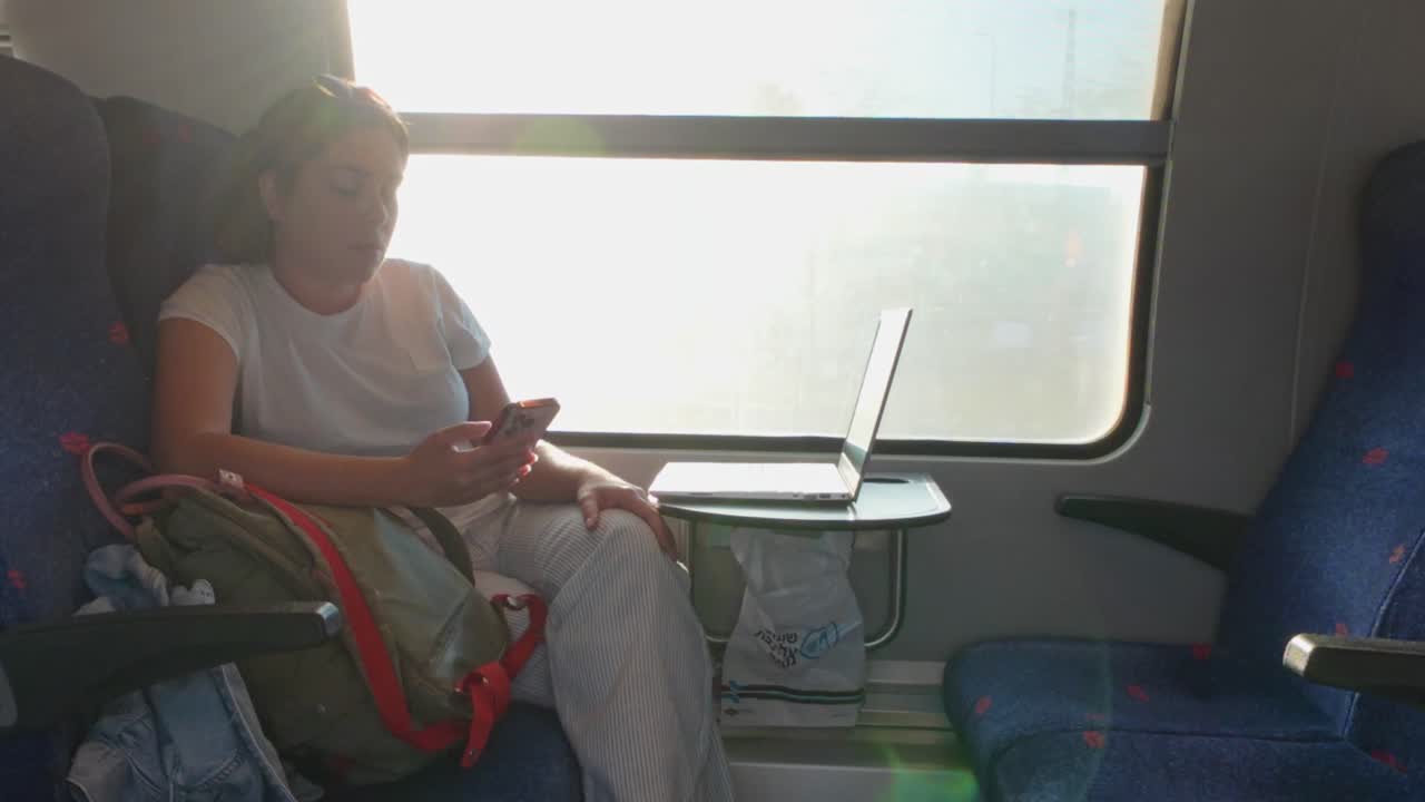 明るい照明が当たった列車の窓際で電話を使用する女性旅行者