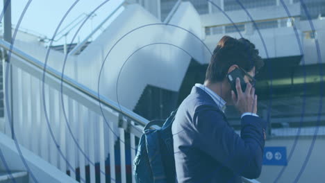 Animation-of-looping-circles-over-asian-man-walking-down-stairs-while-walking-on-smartphone