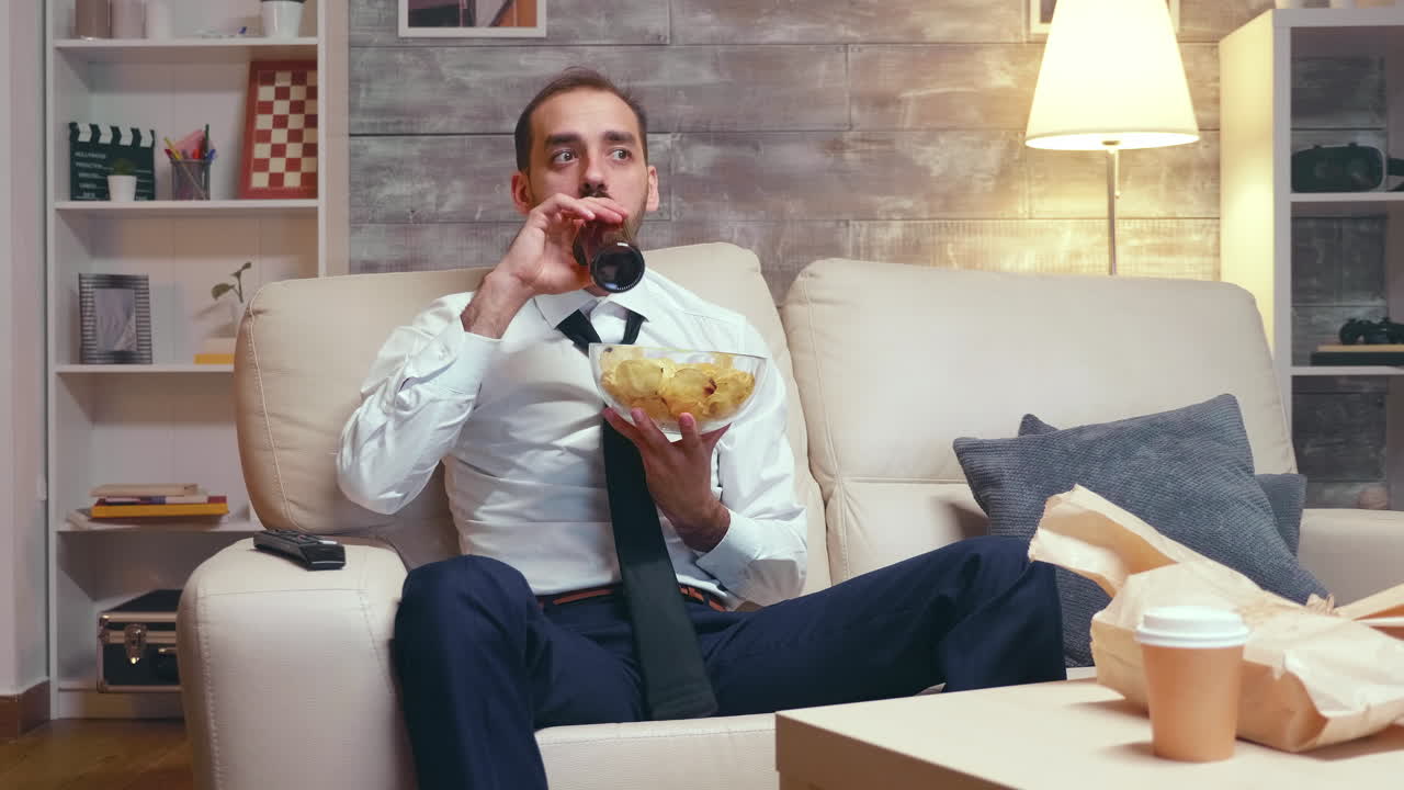 Businessman in formal ear sitting on couch eating chips