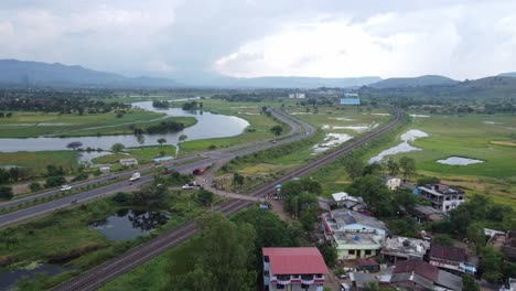 vista aérea de la vía férrea india y la autopista india que corren paralelas en una sola toma con el tren de carga y el paso de la locomotora