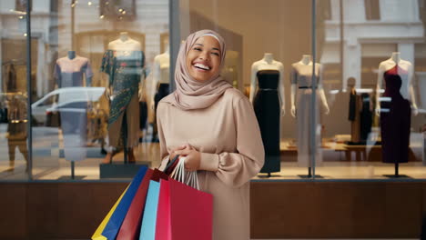 happy woman in hijab with shopping bags in front of a store